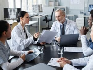 Healthcare professionals in a meeting discussing medical billing strategies, with documents and a laptop on the table, emphasizing teamwork in improving hospital revenue.