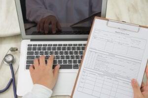 Person typing on laptop with medical billing document and stethoscope, illustrating efficient healthcare billing processes.